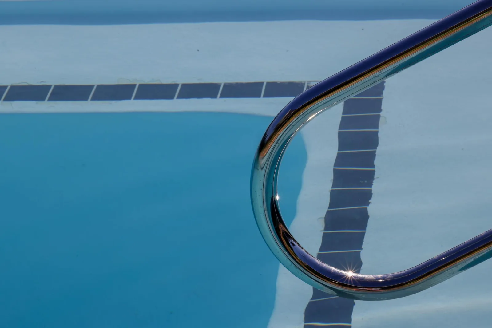 Close-up of a swimming pool with a metal ladder and sunlight reflecting on the water surface.
