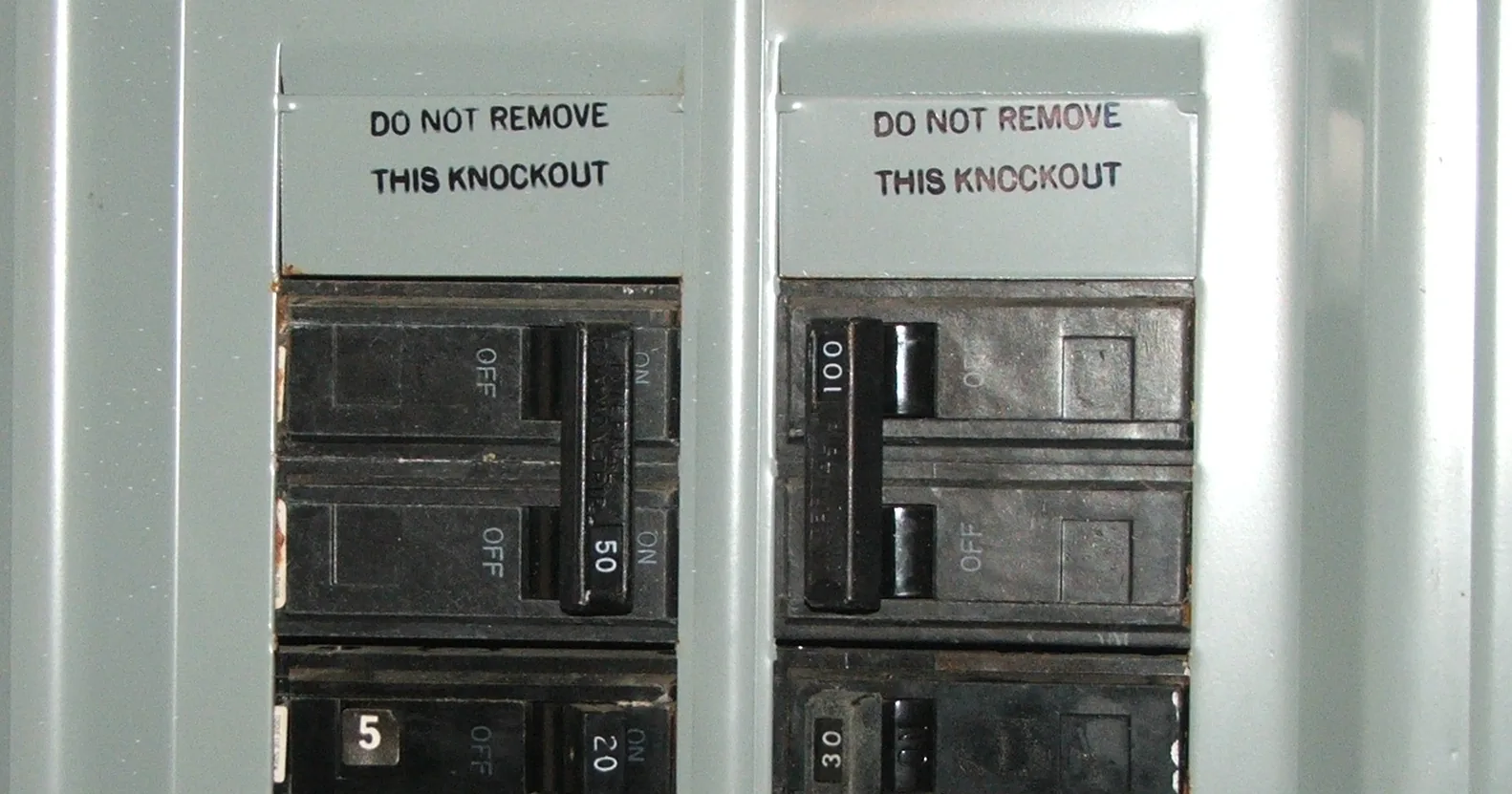 A close view of the top of a residential load center showing a 100 amp double-pole main breaker beside a 50 amp breaker, with the dead front cover in place.
