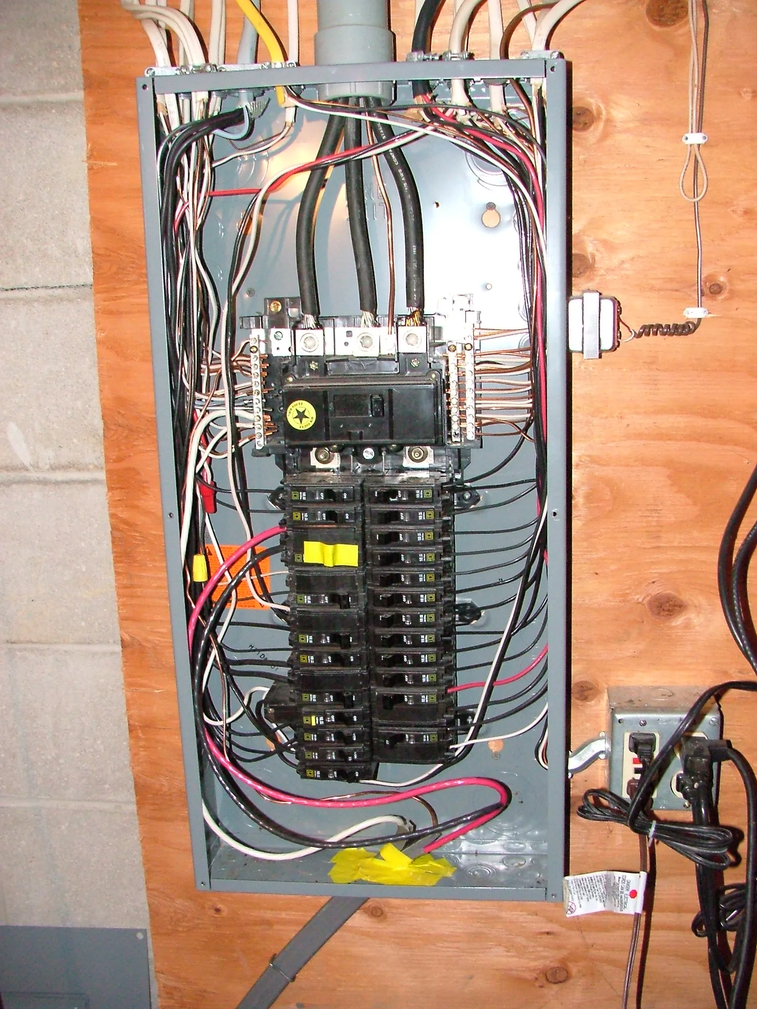 A residential load center with the dead front cover removed, showing the main breaker, two vertical stacks of branch breakers, and black, white and red conductors fanning out to the sides.