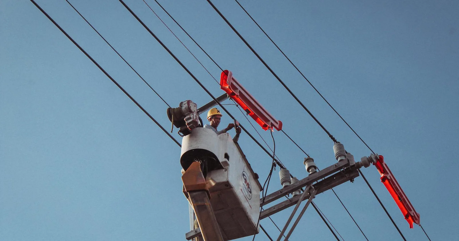 Electrician in a lift repairing overhead power lines on a clear day.