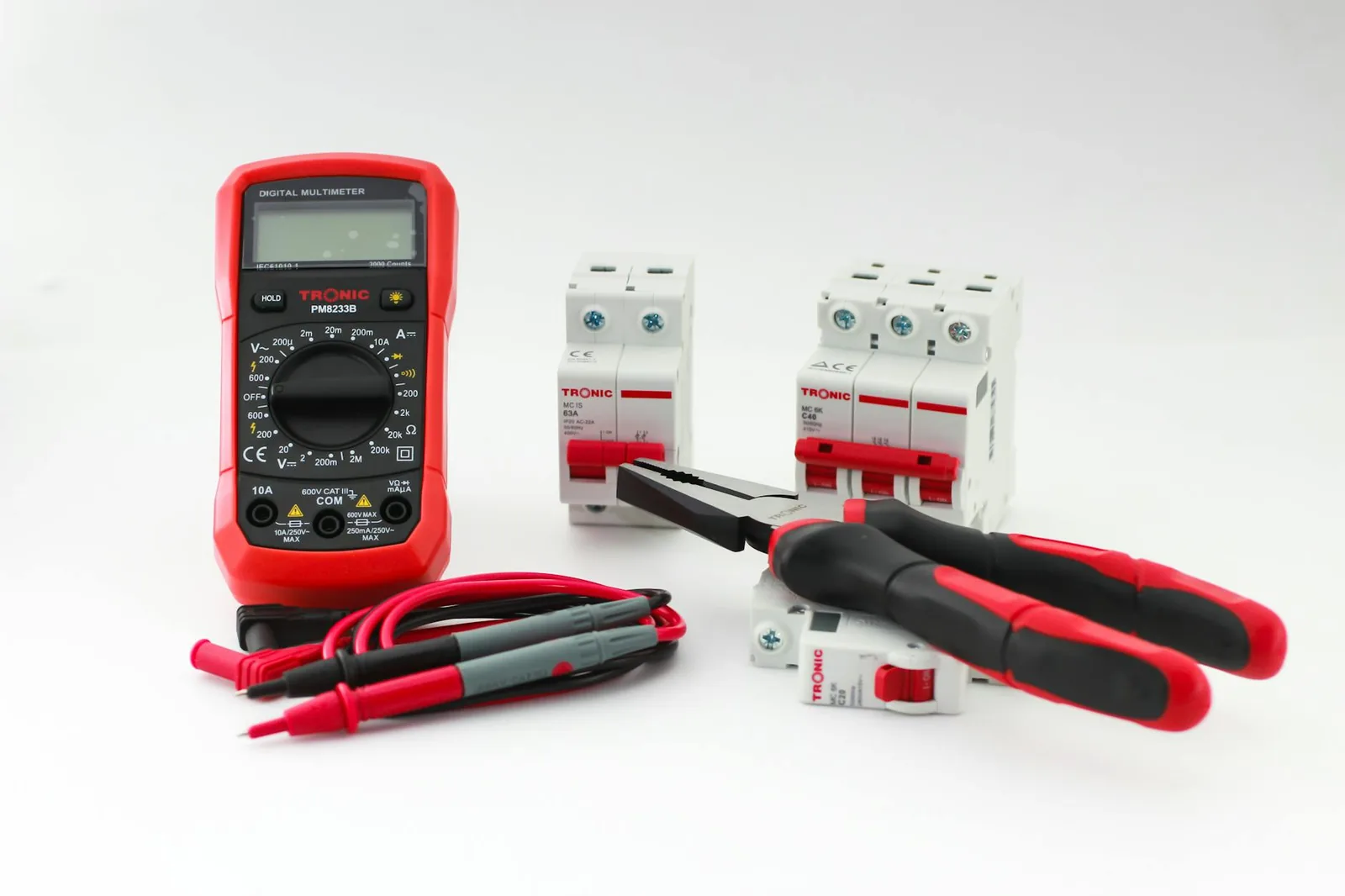 Close-up of a digital multimeter with electrical tools and circuit breakers on a white background.