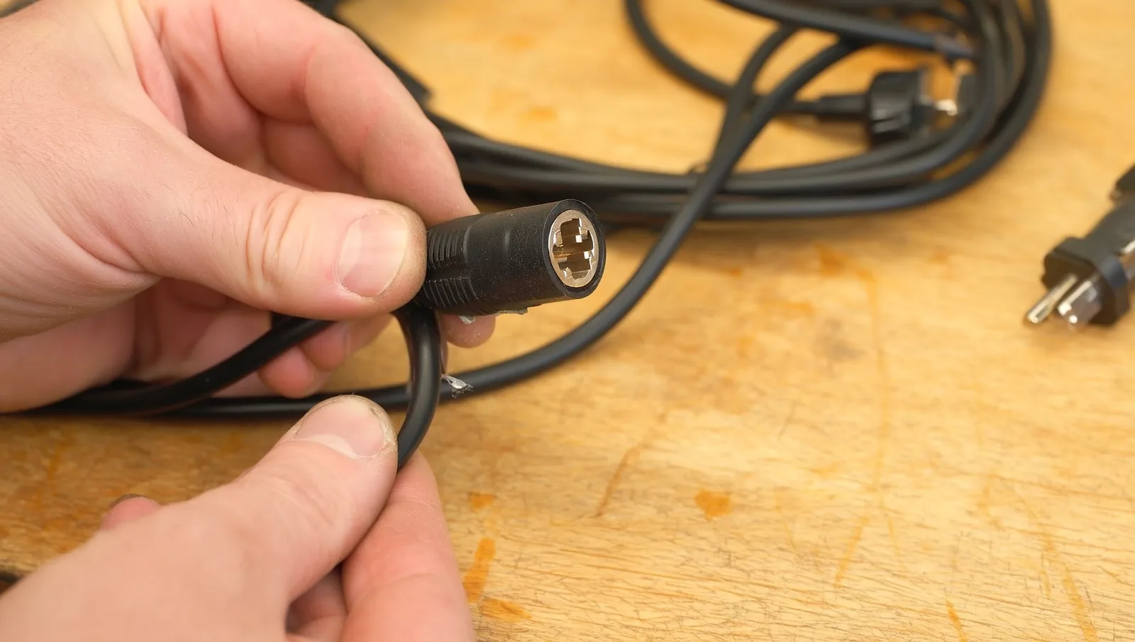 A person's hands inspecting a black extension cord, examining the plug end and insulation for damage on a workbench.
