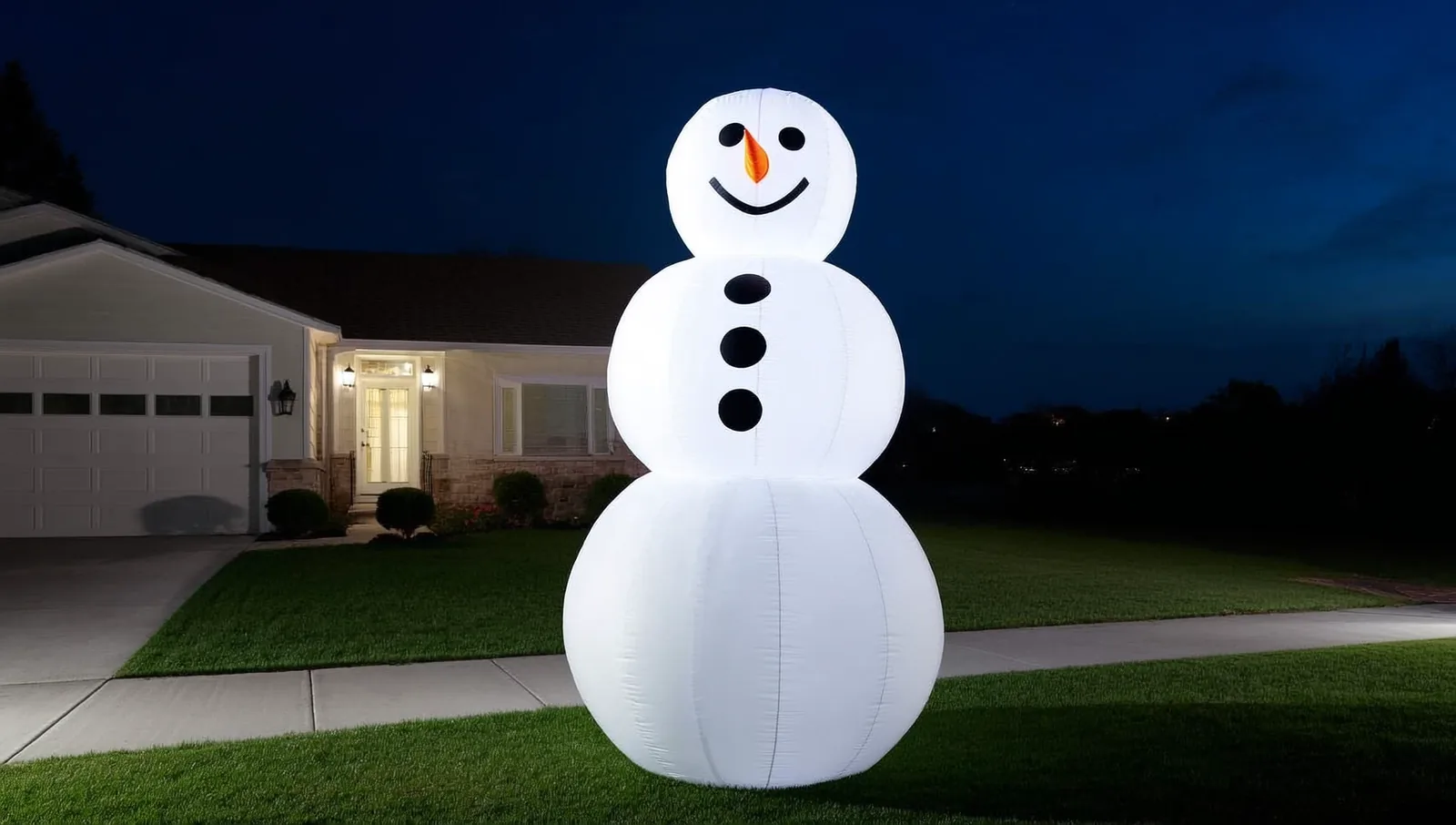An inflatable snowman on a front lawn at night