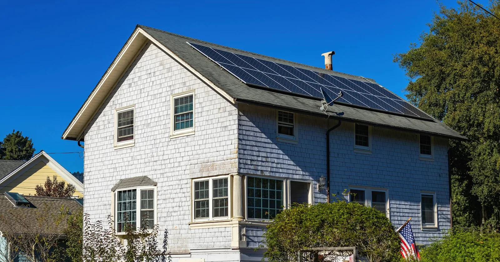A modern two-story home with solar panels on its roof under a clear blue sky.