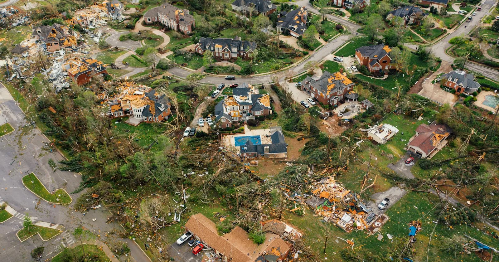 Aerial view of a coastal settlement with destroyed houses and bent uprooted trees after a hurricane.
