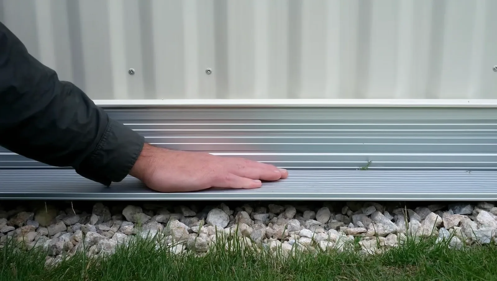 A hand resting flat on metal skirting under a home