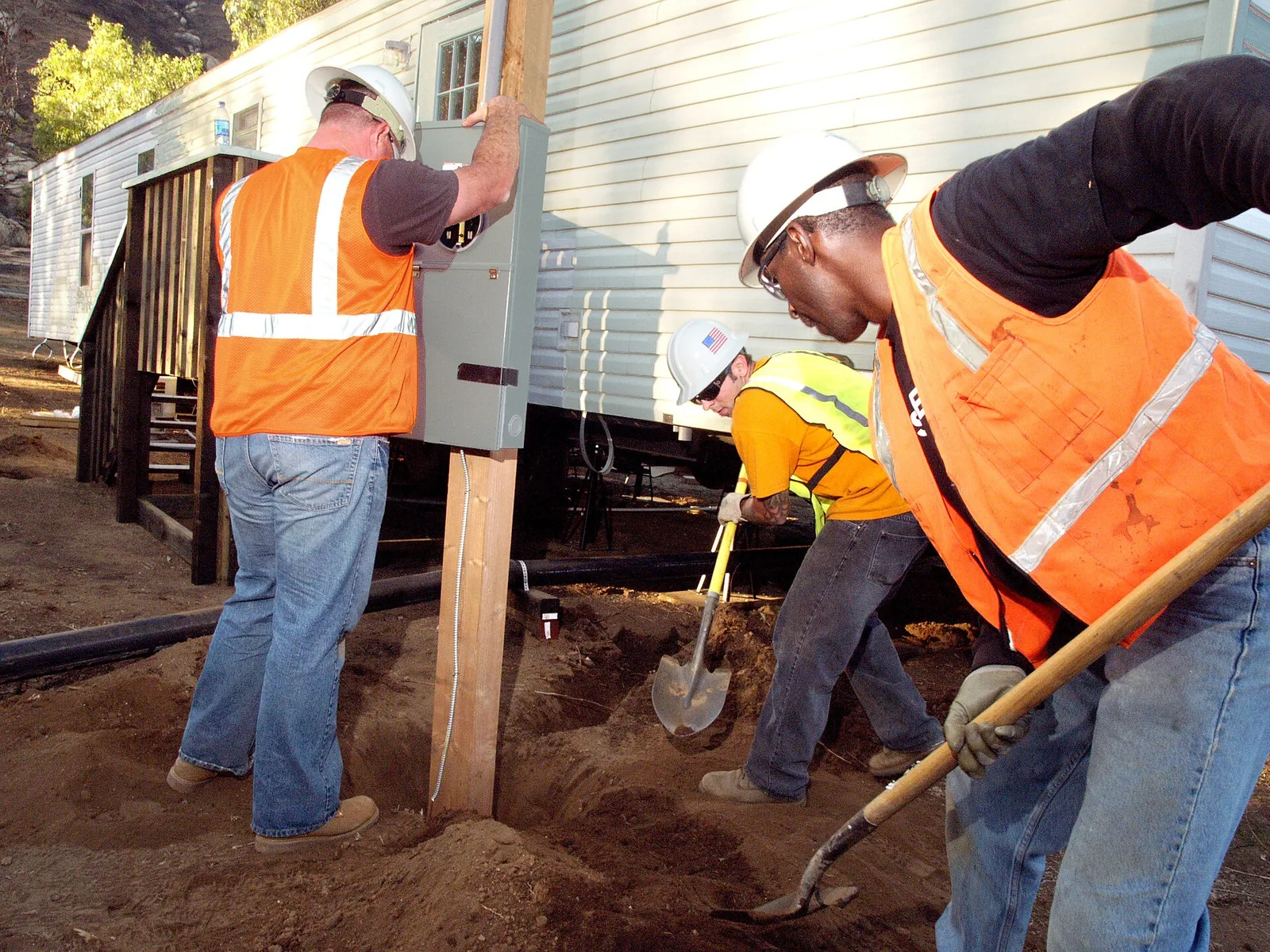 Workers setting an electrical pedestal beside a mobile home