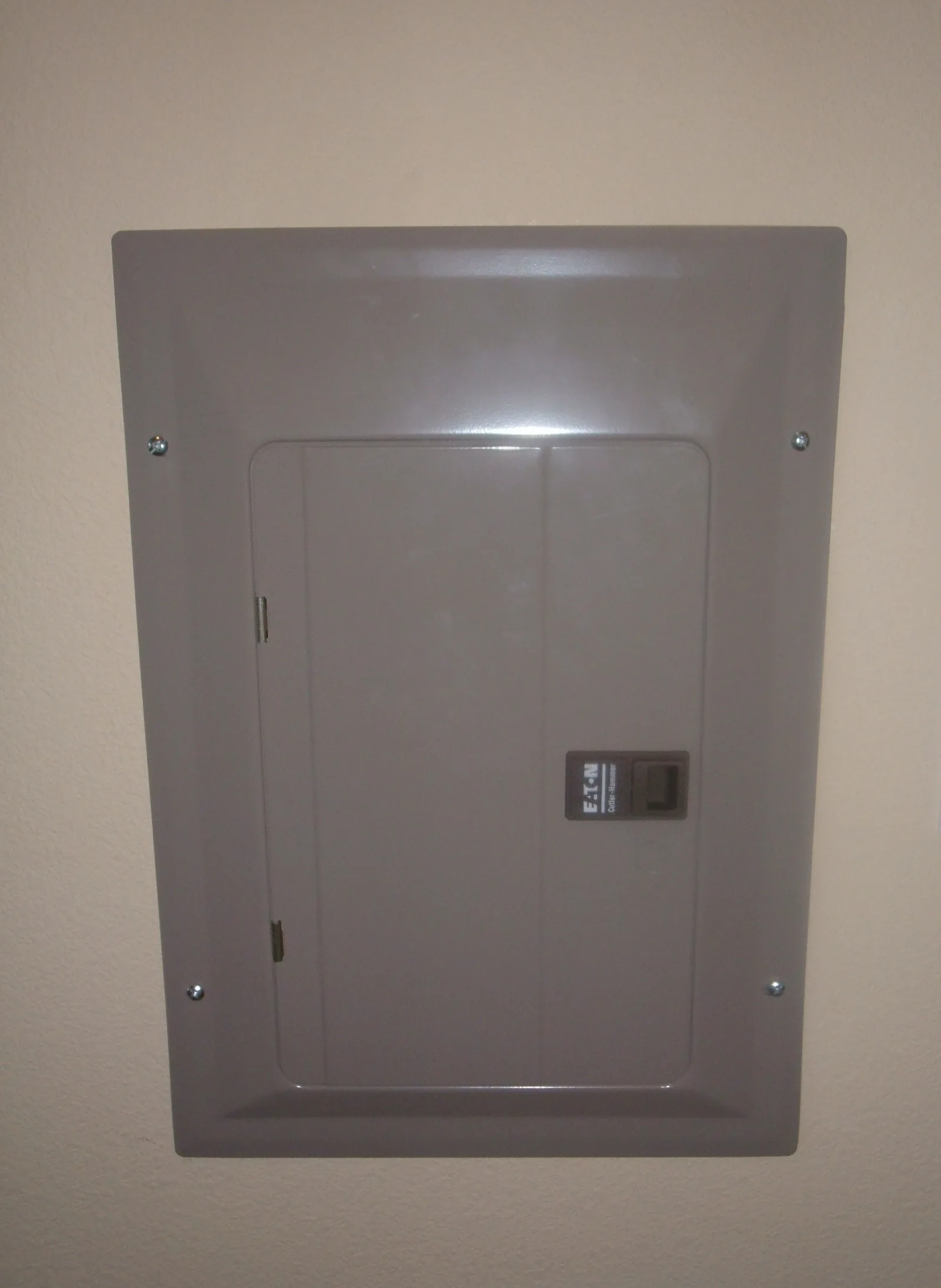 A closed residential Eaton Cutler-Hammer load center mounted flush in an interior wall, with the dead front cover screwed shut and one breaker toggle visible.