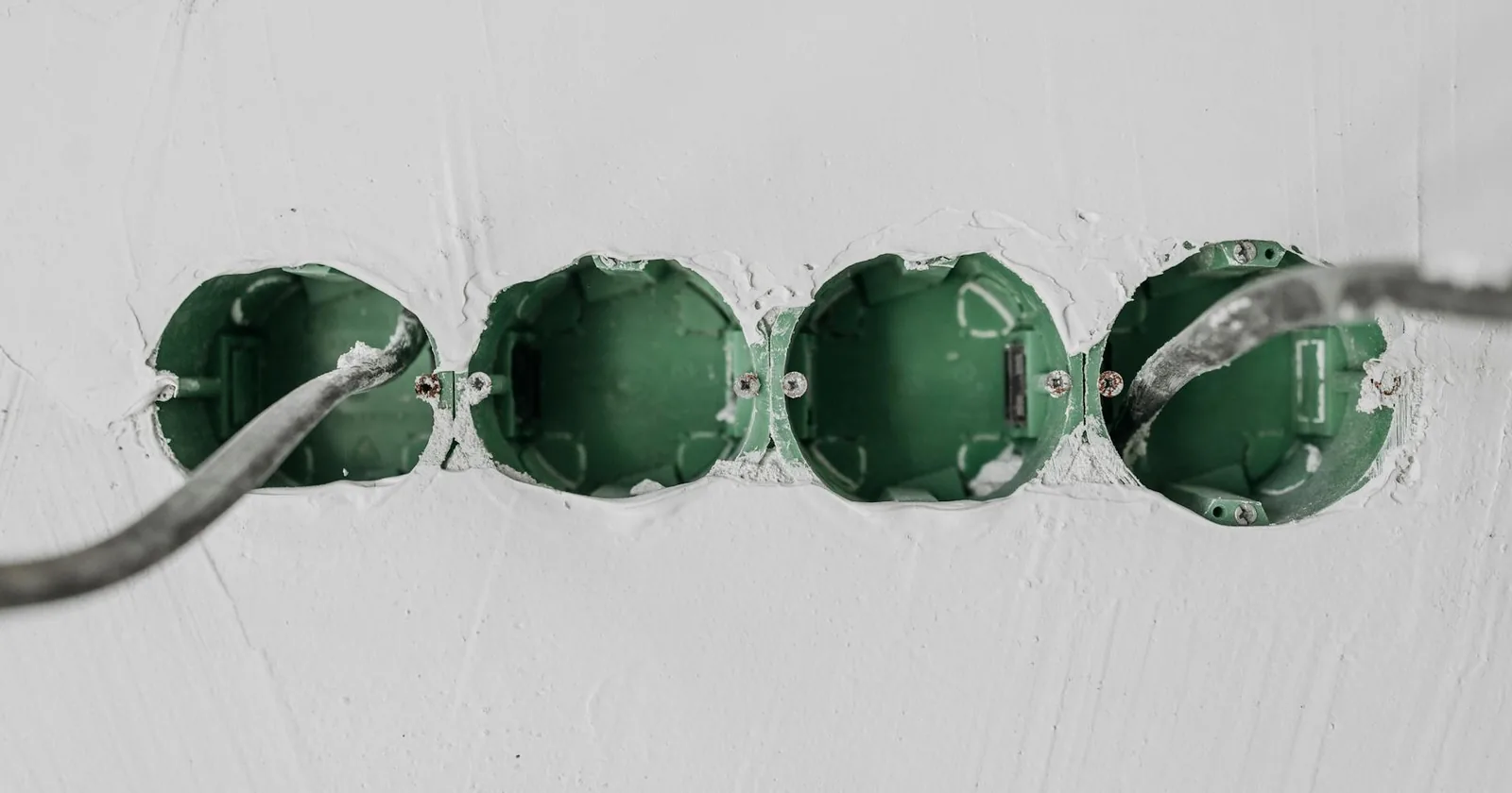 Close-up of green electrical boxes and wiring in a residential wall setup.