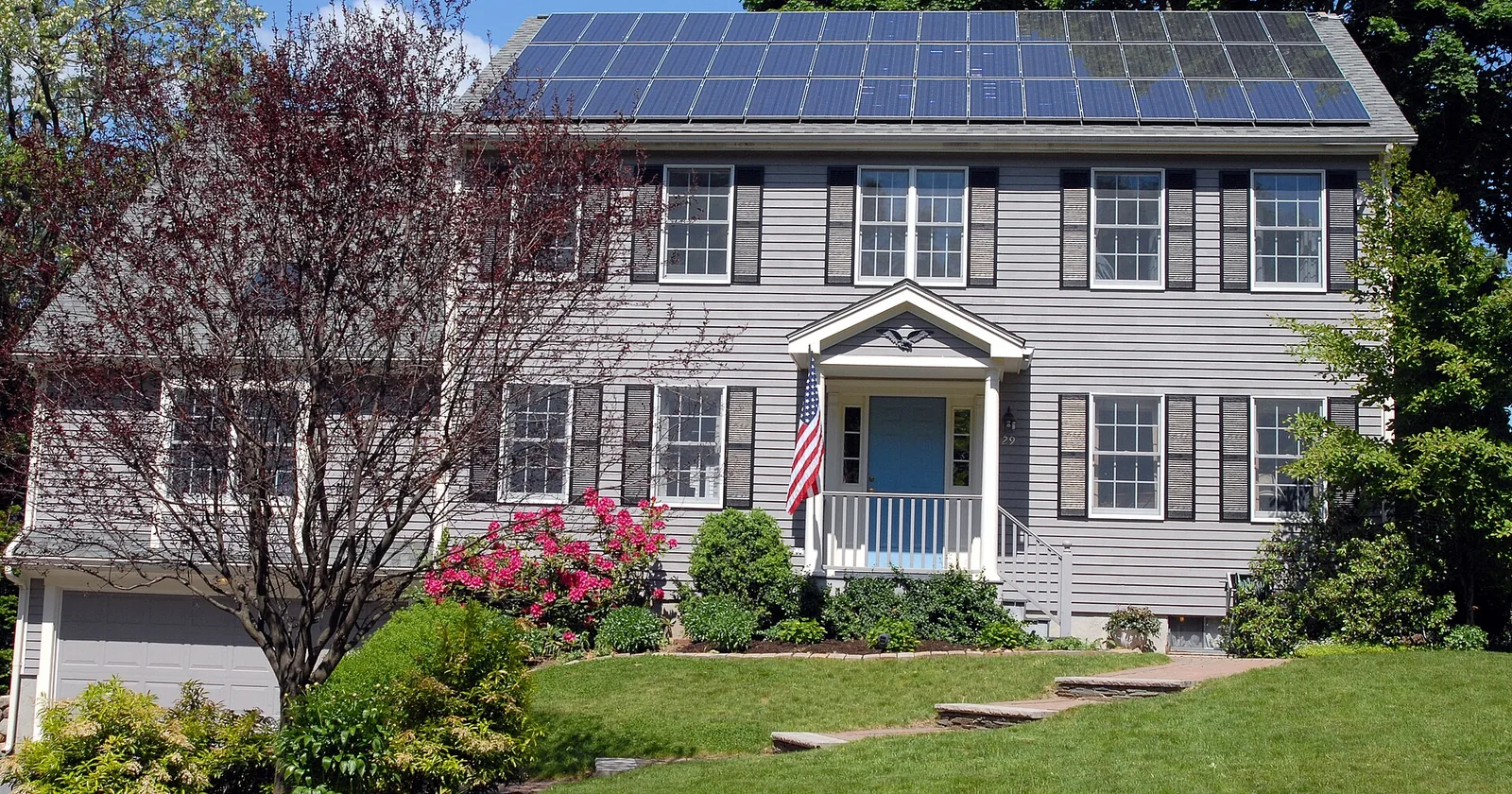 A gray clapboard colonial house with black shutters and a full array of solar panels covering its roof.