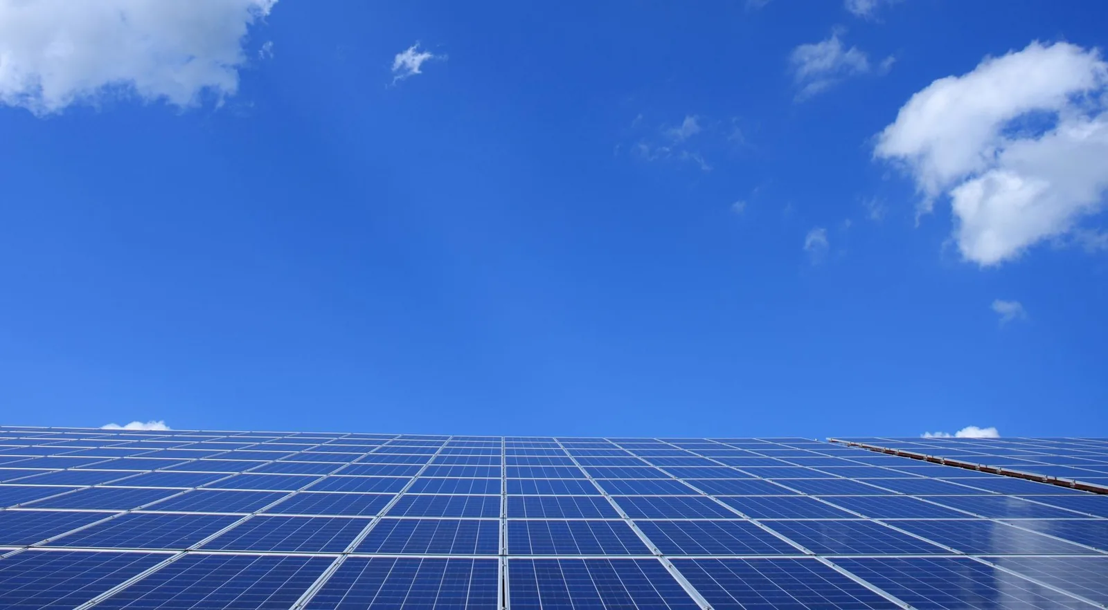 A low angle view along the face of a rooftop solar array, its cells reflecting a bright blue sky.