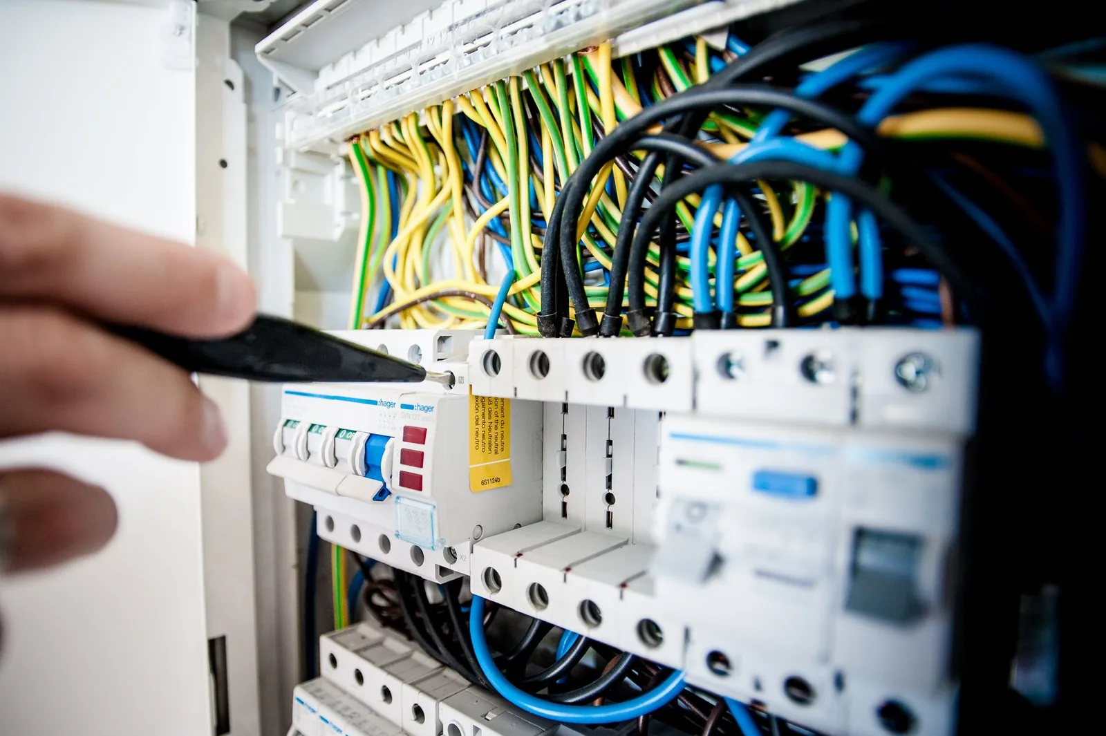 An electrician using a hand tool on an open circuit breaker panel filled with colorful wiring.