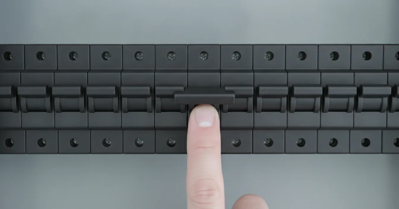 A finger pressing one black circuit breaker flipped to the tripped middle position in a row of breakers inside an open electrical panel.