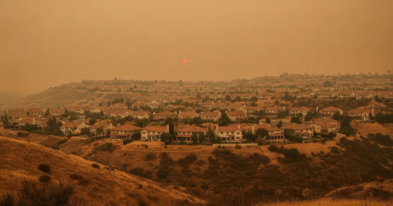 Hillside neighborhood of houses under a smoke-filled sky